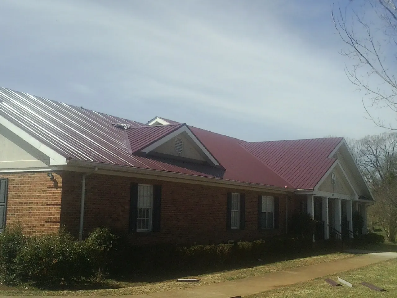 Red metal roof with gabled entries on a long brick building, from a Hail Damage Roof Repair job in Hobart