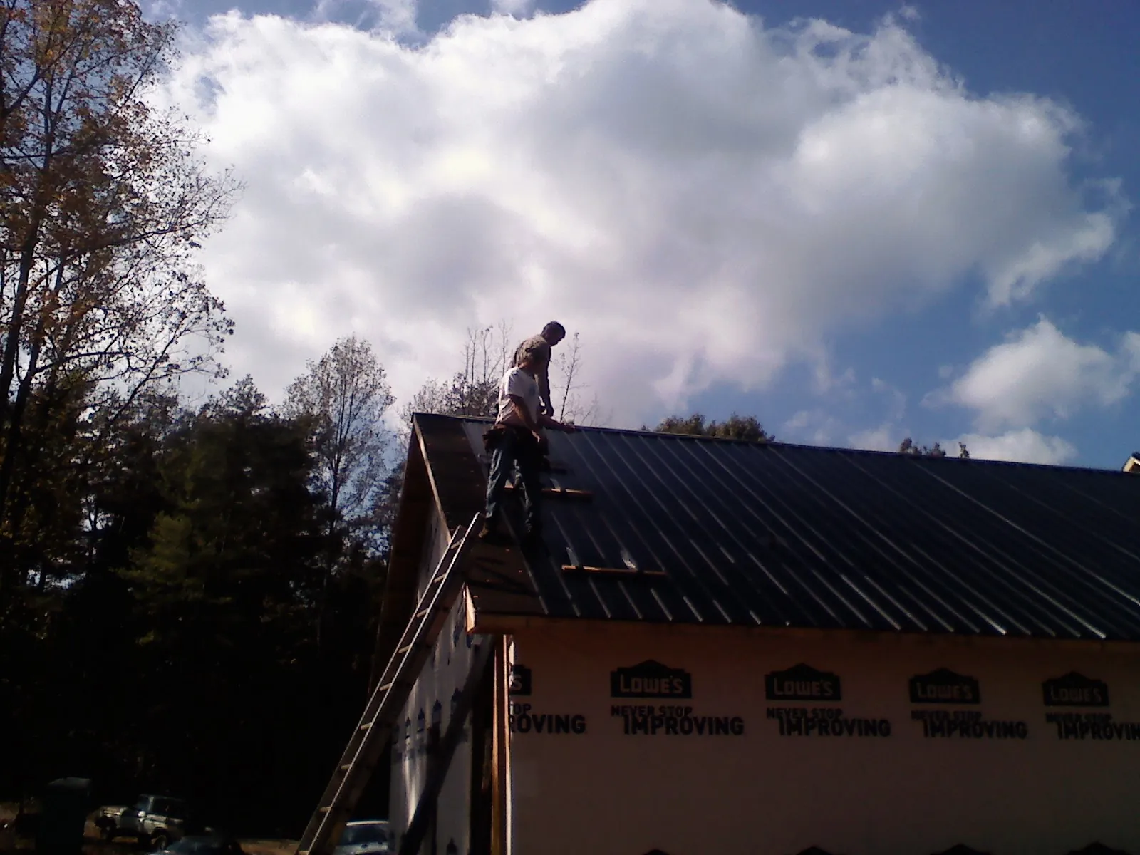 Roofer fastening dark metal panels high against a cloudy sky, from a Roof Inspection job in Hobart