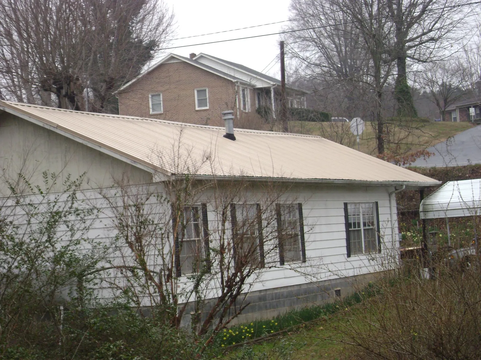 Tan metal roof on a white sided house set into a hillside — Commercial Roofing by Roofing Brothers in Hobart